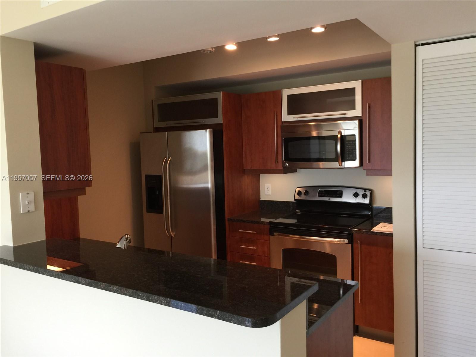 A kitchen features dark wood cabinets, stainless steel appliances, and a black granite countertop — 7350 SW 89th St # 1611S, Miami FL 33156, MIAMI, FL