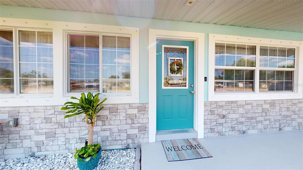 The exterior of a house features a teal front door, stone siding, and a welcome mat — 20407 ALBURY DRIVE, PORT CHARLOTTE, FL
