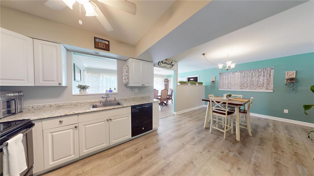 A kitchen with white cabinets and granite countertops opens into a dining area with teal walls — 20407 ALBURY DRIVE, PORT CHARLOTTE, FL