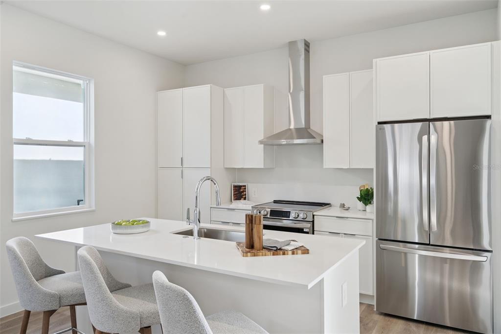 A modern kitchen features white cabinetry, stainless steel appliances, and a central island with seating — 451 SKYFIELD COURT, LADY LAKE, FL