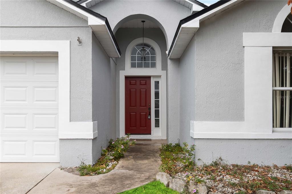 The exterior of a house features a red front door, arched transom window, and garage — 11913 HATCHER CIRCLE, ORLANDO, FL