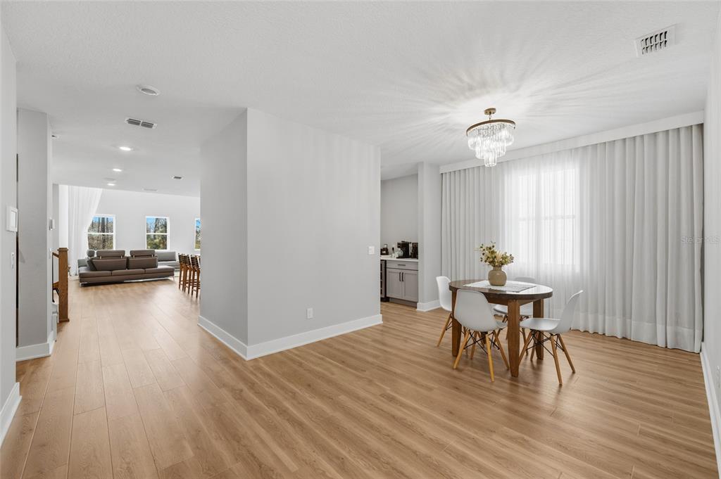 A dining area with a chandelier and table leads to a living room with wood flooring — 17222 DANCY ORANGE COURT, WINTER GARDEN, FL