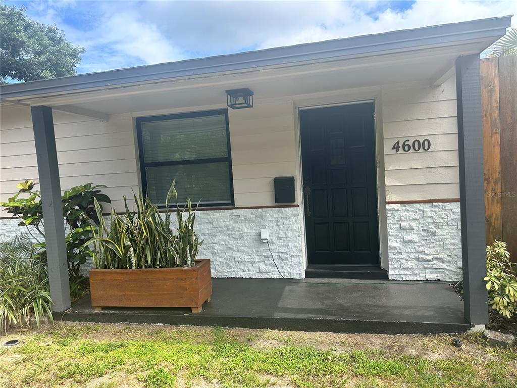 A front porch with a black door, white stone siding, and a wooden planter box — 4600 30TH AVENUE N, ST PETERSBURG, FL