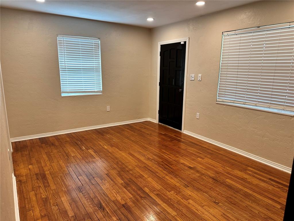 An empty room features hardwood floors, beige walls, two windows with blinds, and a black door — 4600 30TH AVENUE N, ST PETERSBURG, FL