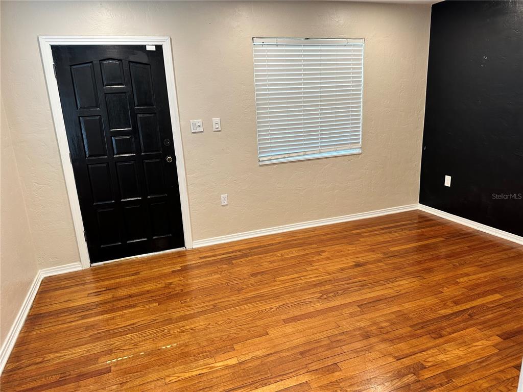 An empty room features hardwood floors, a black door, a window with blinds, and a black wall — 4600 30TH AVENUE N, ST PETERSBURG, FL