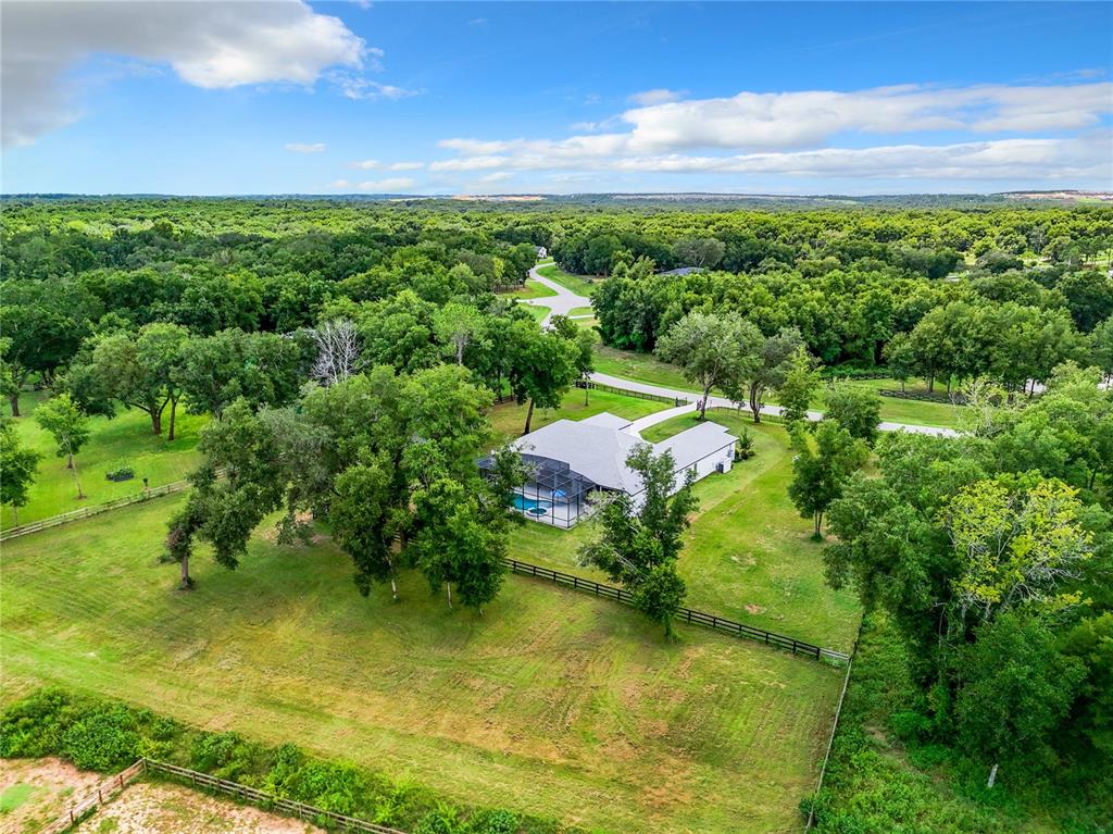 An aerial view shows a house with a pool enclosure surrounded by trees and pastures — 20404 WOLF SPRINGS COURT, CLERMONT, FL