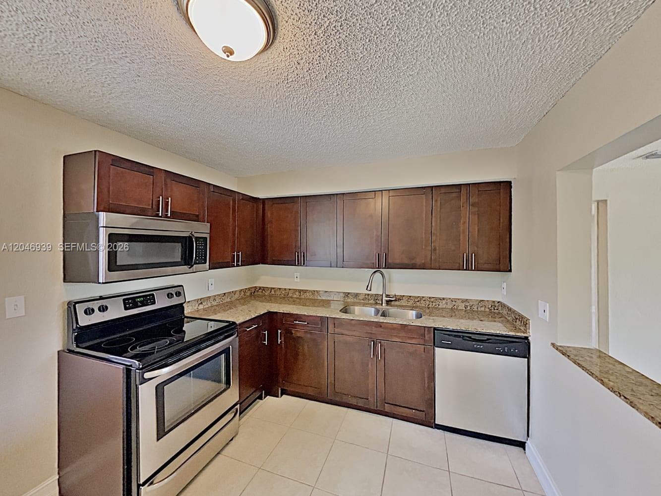 A kitchen features dark wood cabinets, stainless steel appliances, granite countertops, and tile flooring — FORT LAUDERDALE, FL
