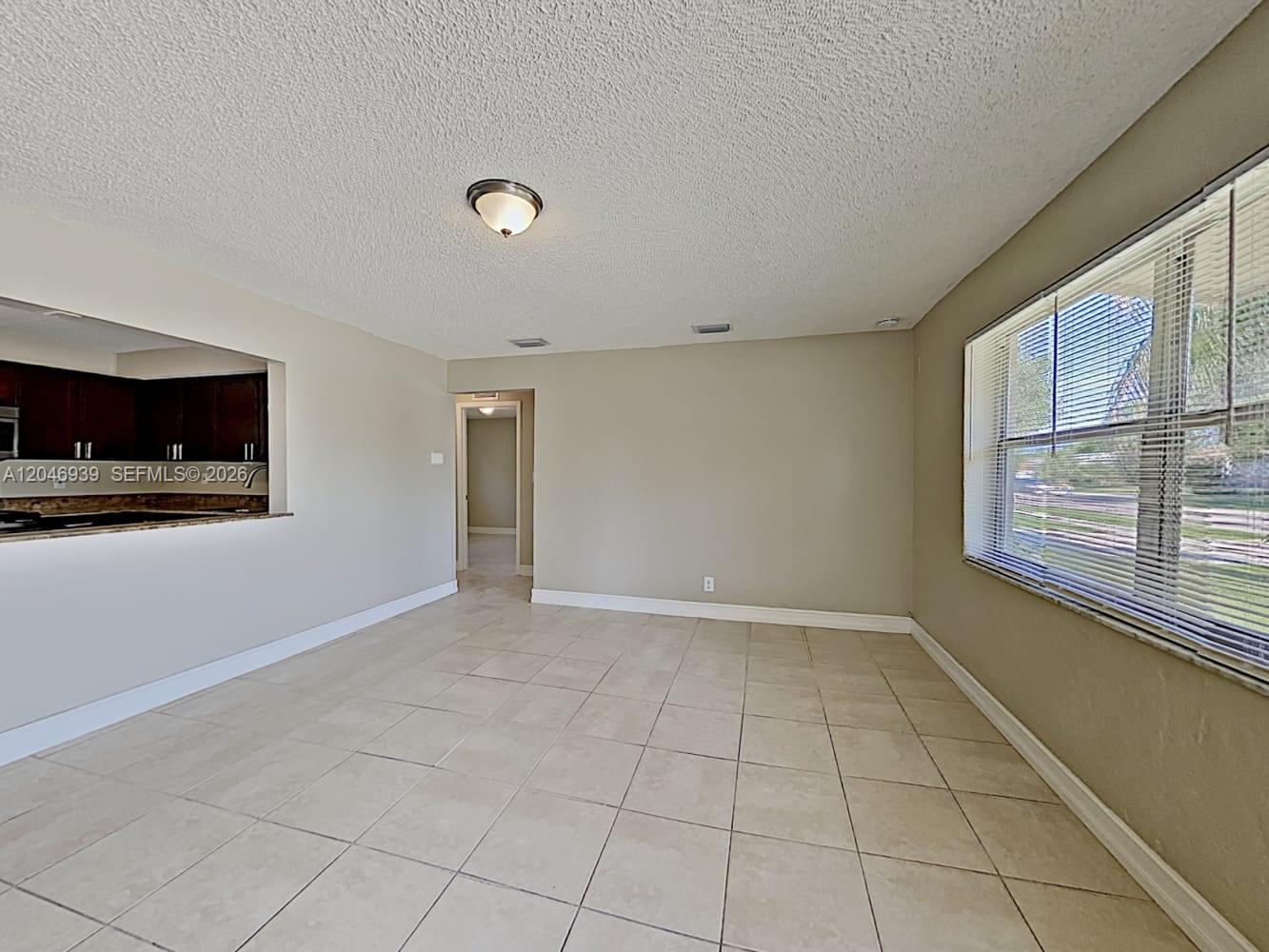 An empty room features beige tile flooring, light-colored walls, and a window with blinds — FORT LAUDERDALE, FL