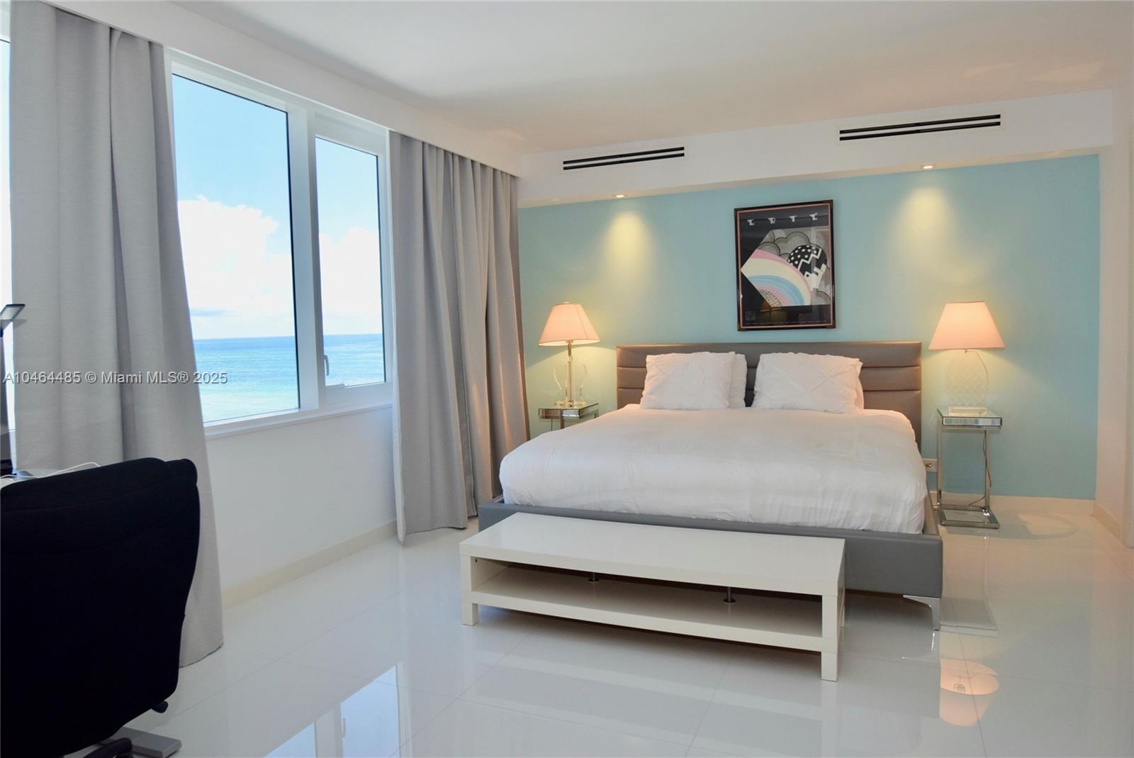 A bedroom features a bed, light blue accent wall, and a view of the ocean — 2301 Collins Ave, Miami Beach FL 33139, MIAMI BEACH, FL