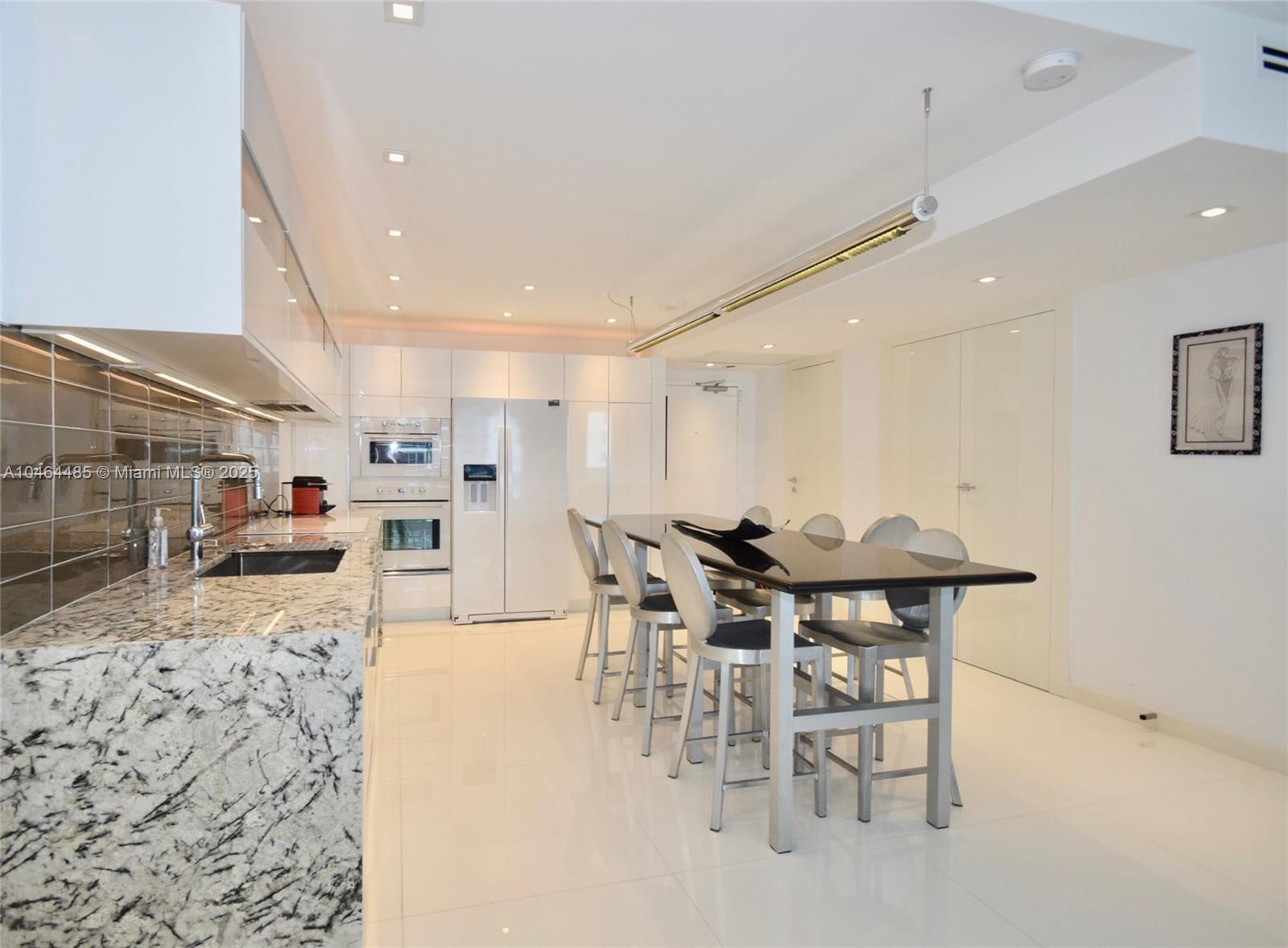 A modern kitchen features white cabinetry, granite countertops, and a black dining table with chairs — 2301 Collins Ave, Miami Beach FL 33139, MIAMI BEACH, FL