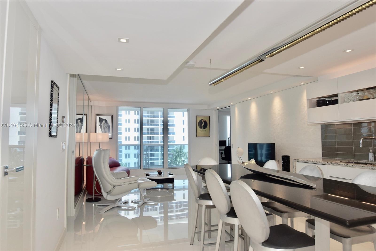 A modern kitchen and dining area features a black island, white chairs, and glossy floors — 2301 Collins Ave, Miami Beach FL 33139, MIAMI BEACH, FL