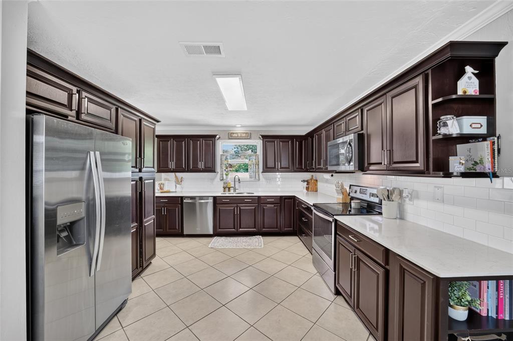 A kitchen with dark wood cabinets, stainless steel appliances, white countertops, and tile flooring — 1861 SE 56TH COURT, OCALA, FL