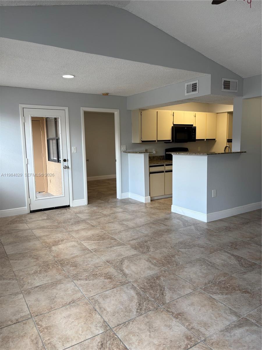 A kitchen with light-colored cabinets and a breakfast bar opens into a tiled living area — 10501 SW 155th Ct # 1124, Miami FL 33196, MIAMI, FL