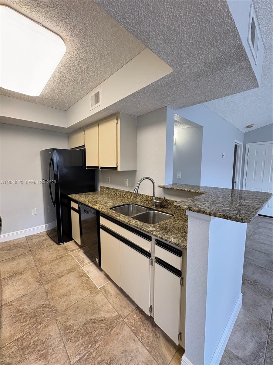 A kitchen features light-colored cabinets, granite countertops, a black refrigerator, and tiled flooring — 10501 SW 155th Ct # 1124, Miami FL 33196, MIAMI, FL