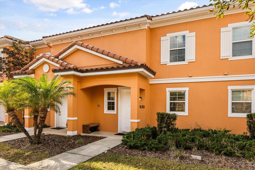 A two-story orange stucco townhouse with a tiled roof, palm tree, and front entryway — 2630 CORVETTE LANE, KISSIMMEE, FL