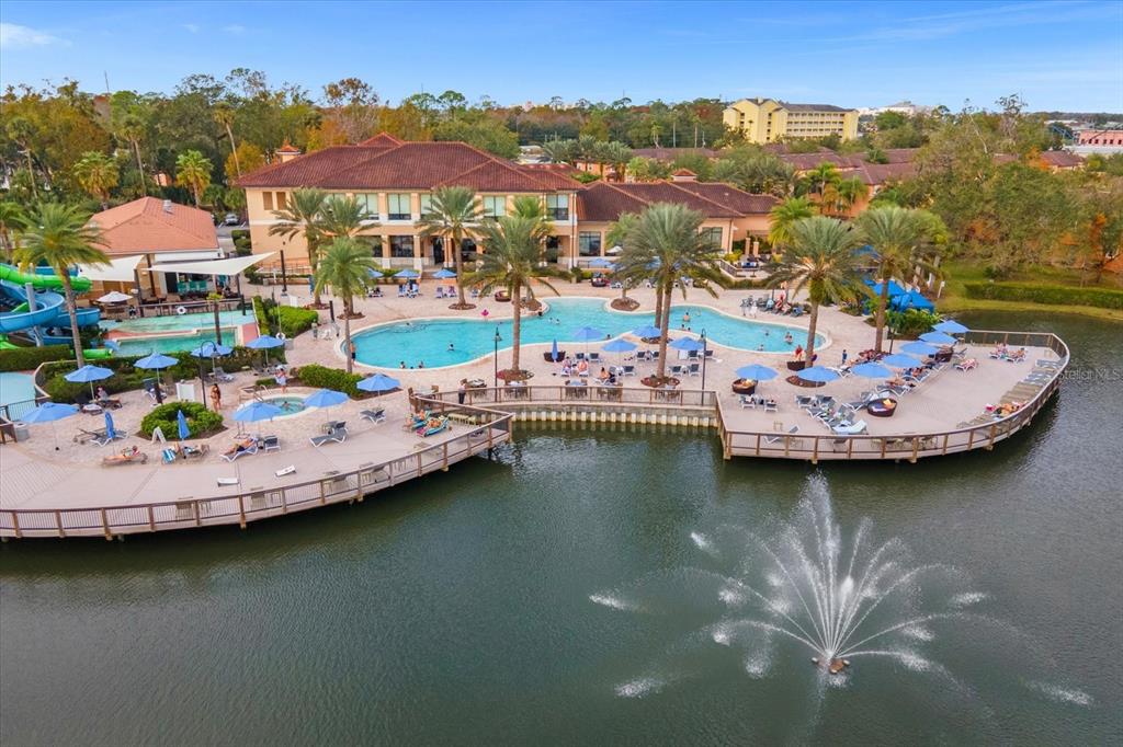 An aerial view of a resort-style swimming pool and deck area beside a lake — 2630 CORVETTE LANE, KISSIMMEE, FL