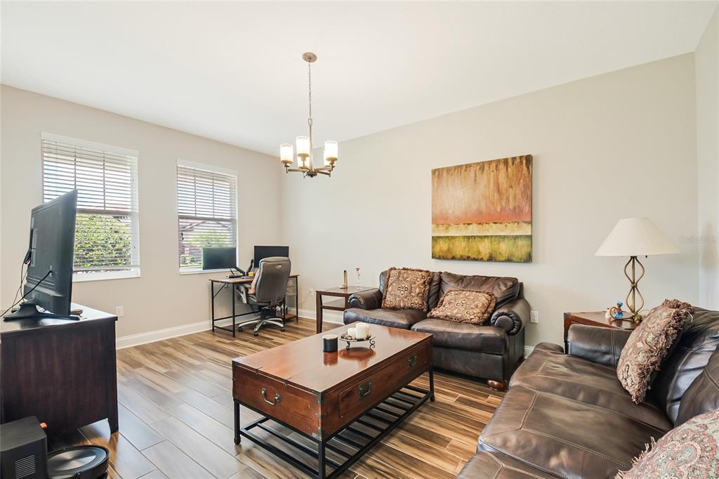 A living room with wood-look tile floors, leather furniture, a coffee table, and a desk area — 12278 NORTHOVER LOOP, ORLANDO, FL