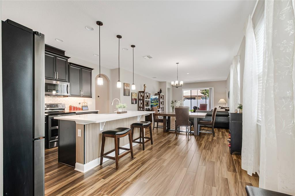 An open-concept kitchen and dining area features dark cabinetry, a slatted island, and wood-look flooring — 12278 NORTHOVER LOOP, ORLANDO, FL