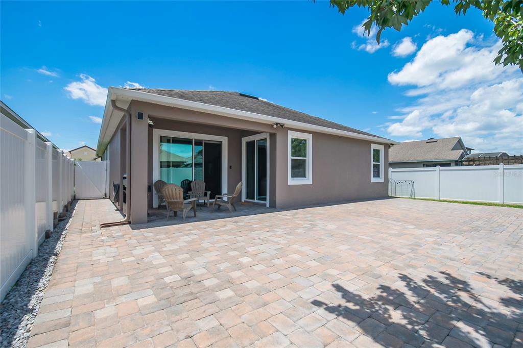 A paved patio sits behind a house with a covered porch and white vinyl fencing — 12278 NORTHOVER LOOP, ORLANDO, FL