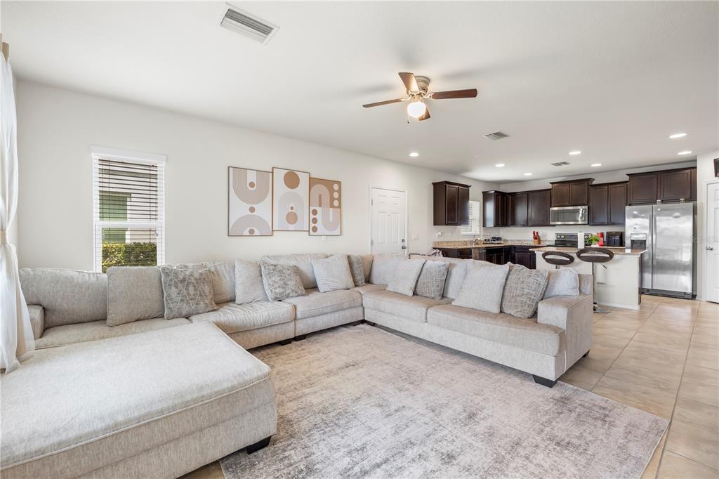 A large sectional sofa sits on a rug in an open-concept living room and kitchen — 9335 AMERICAN HICKORY LANE, RIVERVIEW, FL