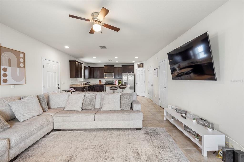 A living room with a sectional sofa, a wall-mounted television, and an open kitchen — 9335 AMERICAN HICKORY LANE, RIVERVIEW, FL