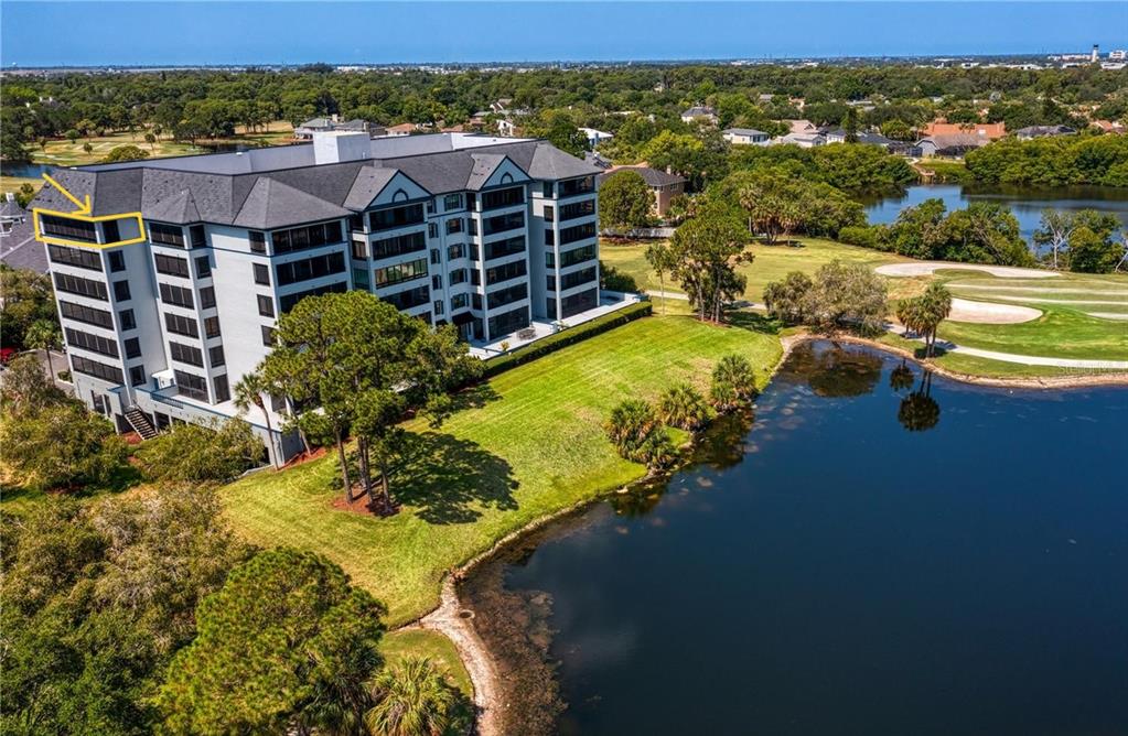 An aerial view of a multi-story apartment building situated next to a lake and golf course — 14810 RUE DE BAYONNE UNIT 7G, CLEARWATER, FL