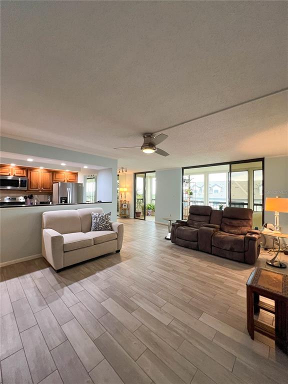 A living room features light wood-look tile flooring, a beige loveseat, and brown reclining chairs — 14810 RUE DE BAYONNE UNIT 7G, CLEARWATER, FL