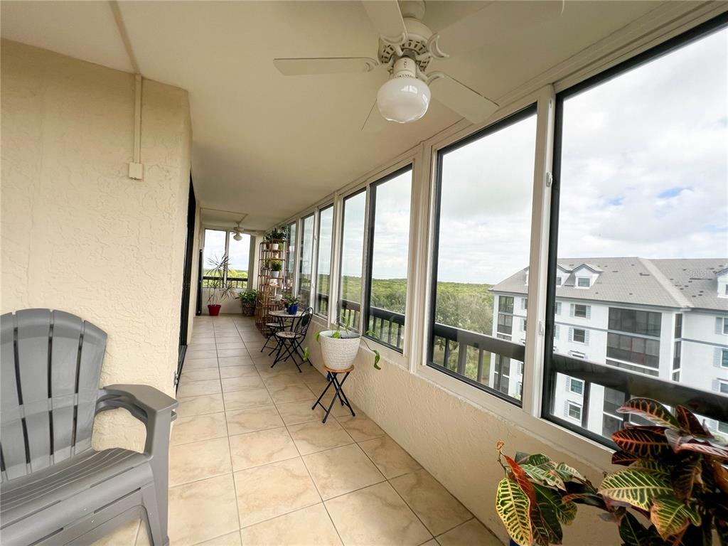A tiled sunroom features a ceiling fan, large windows, and a view of nearby buildings — 14810 RUE DE BAYONNE UNIT 7G, CLEARWATER, FL
