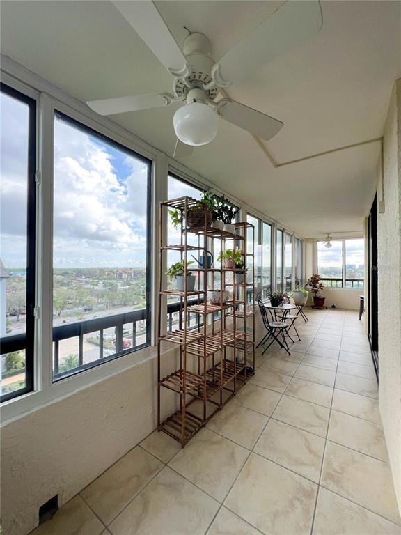 A sunroom features tile flooring, a ceiling fan, large windows, and a wooden plant stand — 14810 RUE DE BAYONNE UNIT 7G, CLEARWATER, FL