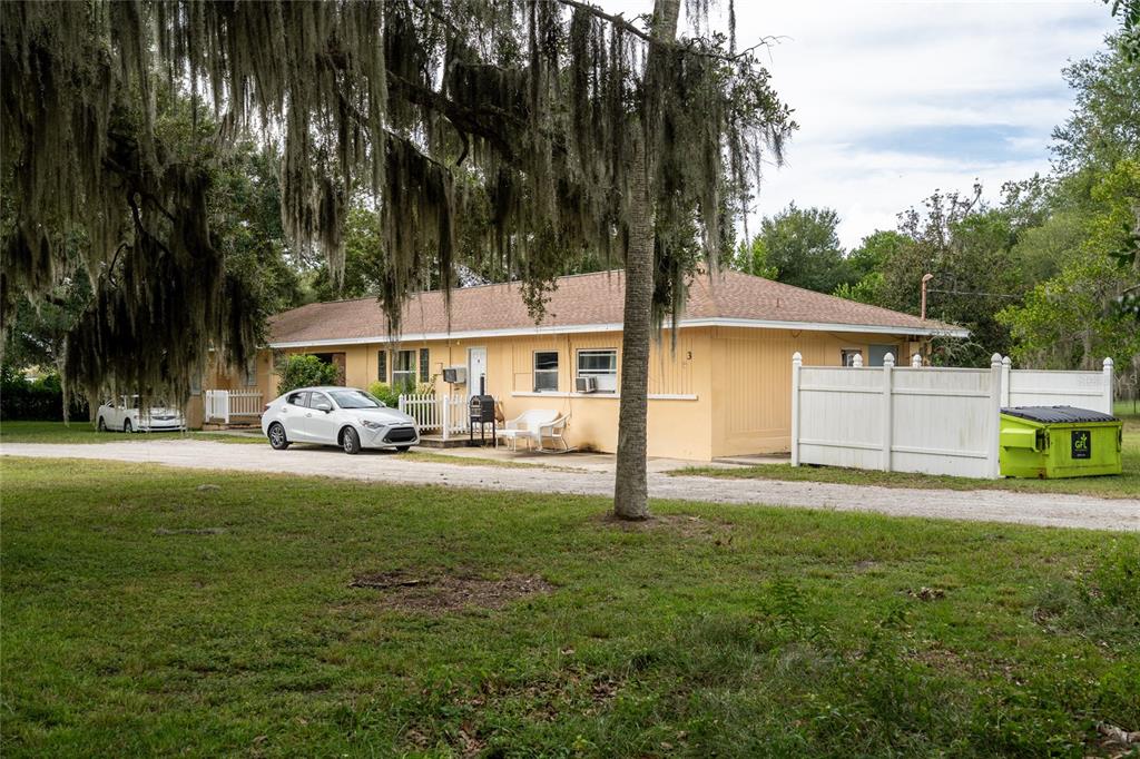 A single-story yellow house with a brown roof sits on a gravel driveway near trees — 124 S CHARLES RICHARD BEALL BOULEVARD, DEBARY, FL