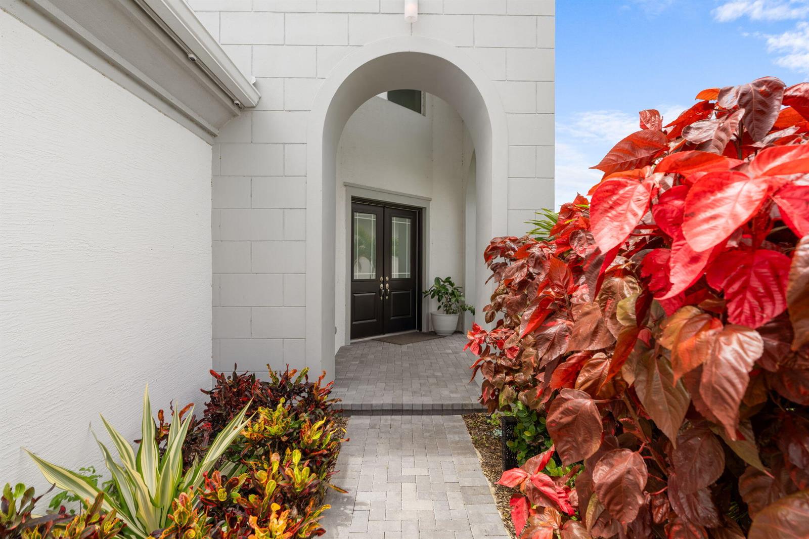 A paved walkway leads to a dark double-door entrance under a white arched entryway — 14070 Spruce Pine Drive, Westlake FL 33470, WESTLAKE, FL