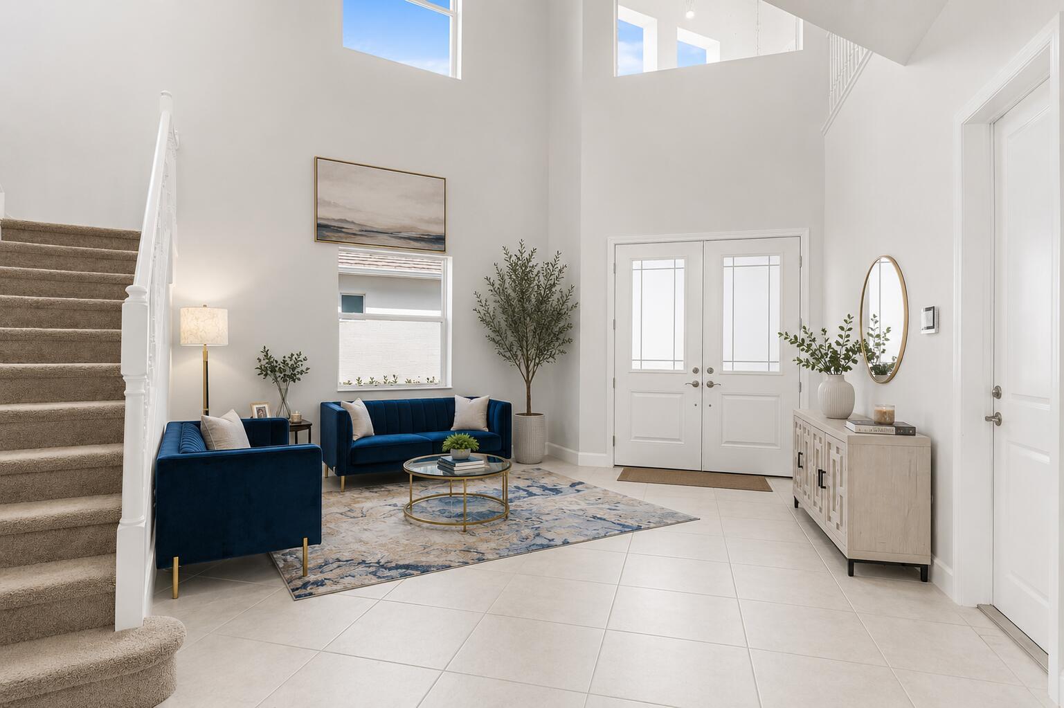 A bright, high-ceilinged foyer features a blue velvet sofa, a staircase, and tile flooring — 14070 Spruce Pine Drive, Westlake FL 33470, WESTLAKE, FL