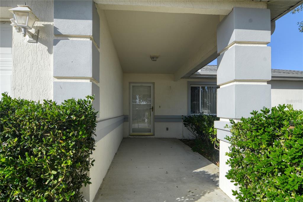 A covered entryway features a concrete porch, two large pillars, and a glass storm door — 9832 SW 61ST COURT, OCALA, FL