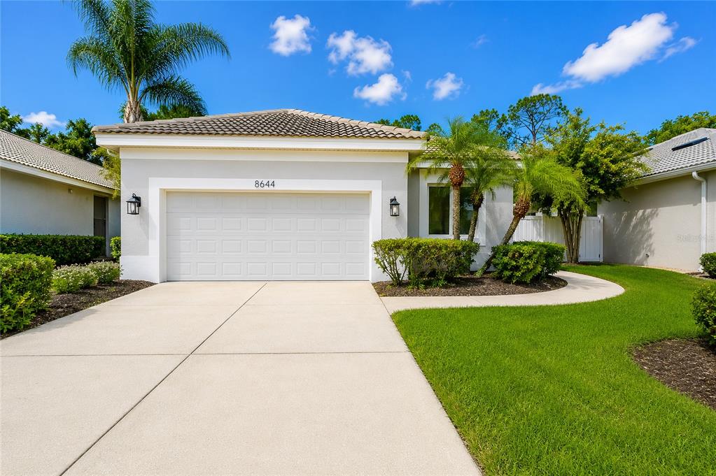 A single-story house with a white garage door, light-colored stucco walls, and a tiled roof — 8644 54TH AVENUE CIRCLE E, BRADENTON, FL