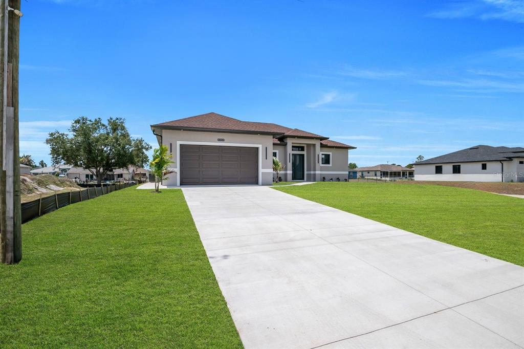 A single-story house with a brown garage door and a concrete driveway under blue skies — 3115 2ND STREET SW, LEHIGH ACRES, FL