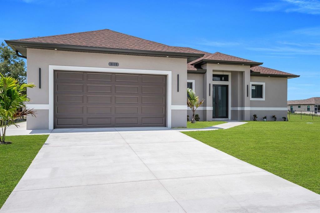 A modern single-story house features a two-car garage, a covered entryway, and a concrete driveway — 3115 2ND STREET SW, LEHIGH ACRES, FL