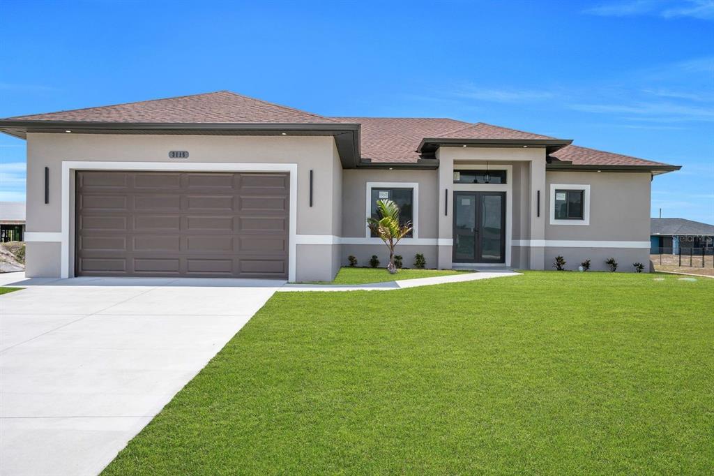 A single-story house with a two-car garage, gray stucco exterior, and a front lawn — 3115 2ND STREET SW, LEHIGH ACRES, FL