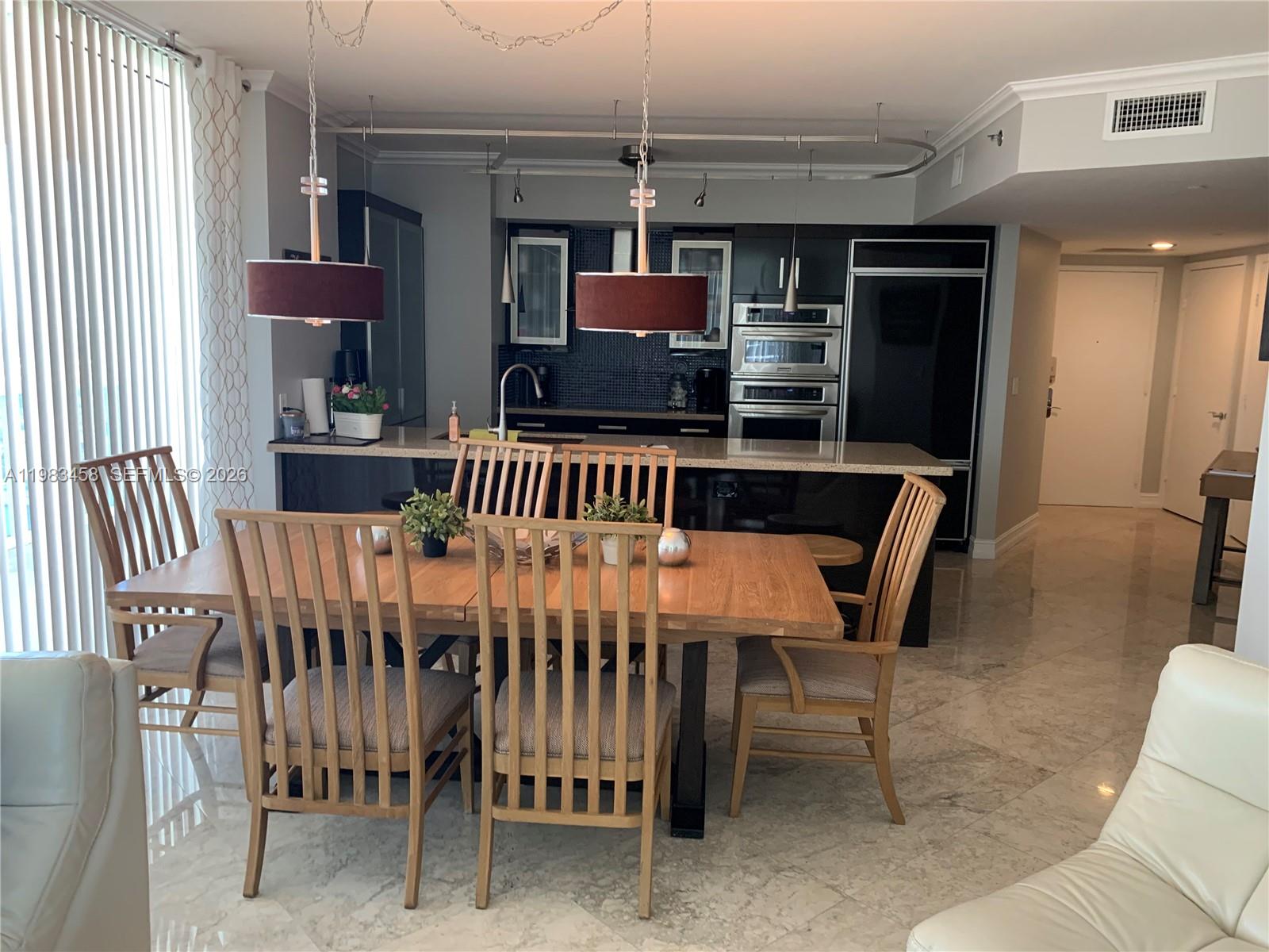 A dining area with a wooden table and chairs sits in front of a modern kitchen — 1830 S Ocean Dr # 4006, Hallandale Beach FL 33009, HALLANDALE BEACH, FL