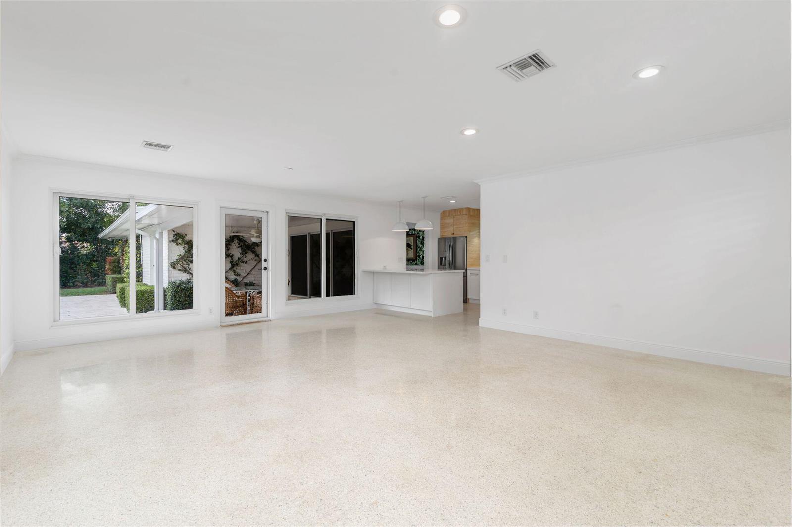 A spacious, white-walled room features polished terrazzo flooring, recessed lighting, and a kitchen peninsula — 246 Gray Street, West Palm Beach FL 33405, WEST PALM BEACH, FL