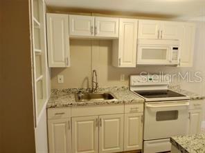 A kitchen features white cabinets, a stainless steel sink, and white appliances — 4204 N MANHATTAN AVENUE, TAMPA, FL