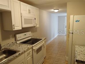 A kitchen features white cabinets, granite-look countertops, a white stove, and a white refrigerator — 4204 N MANHATTAN AVENUE, TAMPA, FL