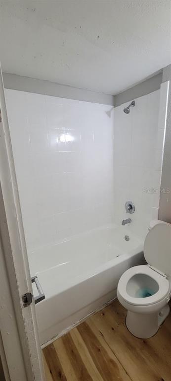 A bathroom features a white tiled shower-tub combination next to a white toilet on wood flooring — 4204 N MANHATTAN AVENUE, TAMPA, FL