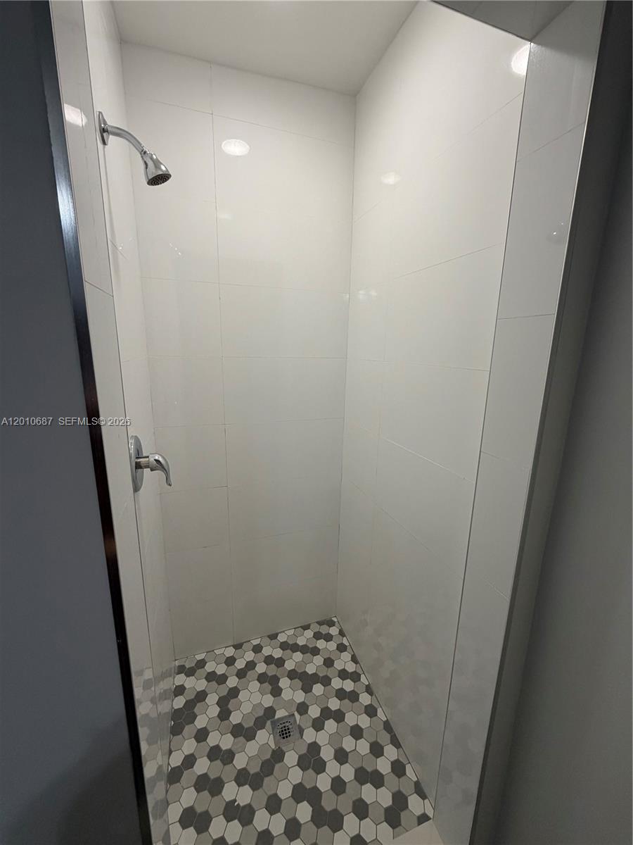 A walk-in shower features white tiled walls and a gray and white hexagonal floor — 2433 NW 96th St # B, Miami FL 33147, MIAMI, FL