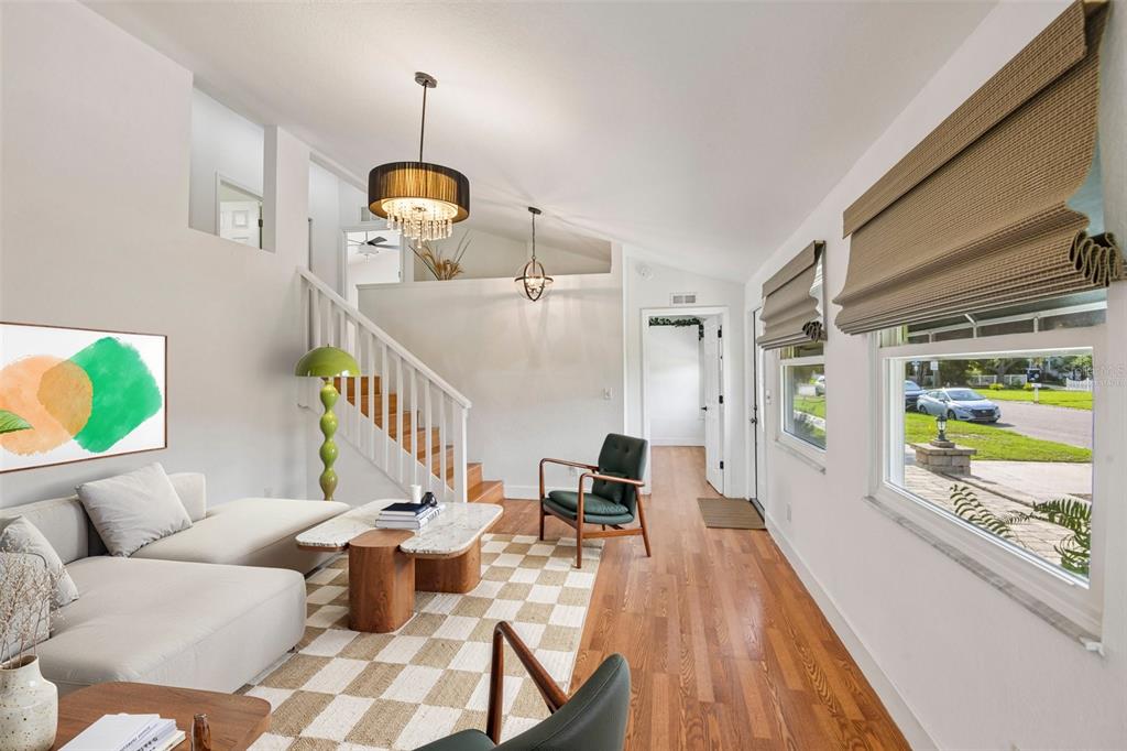 A living room features a white sectional sofa, a checkered rug, and a wooden staircase — 5731 28TH AVENUE S, GULFPORT, FL