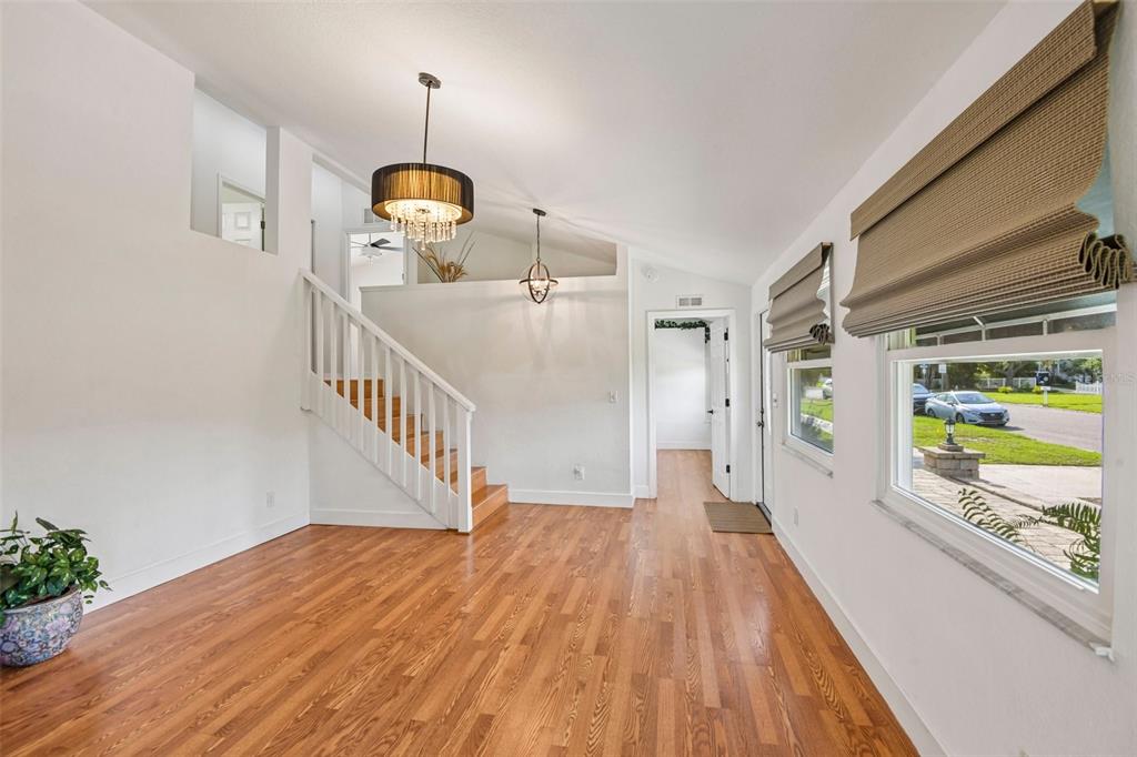 A bright entryway features hardwood floors, a staircase with white railings, and two hanging chandeliers — 5731 28TH AVENUE S, GULFPORT, FL