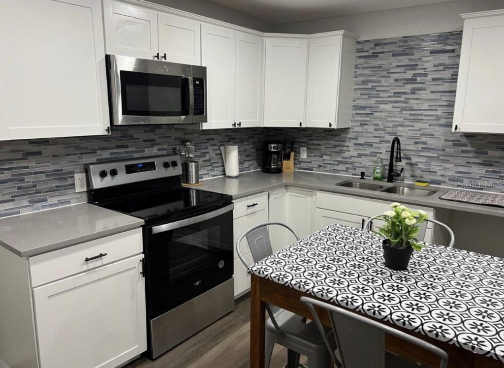 A kitchen features white cabinets, gray countertops, a stainless steel stove, and a tiled backsplash — 10015 LINDA STREET, GIBSONTON, FL