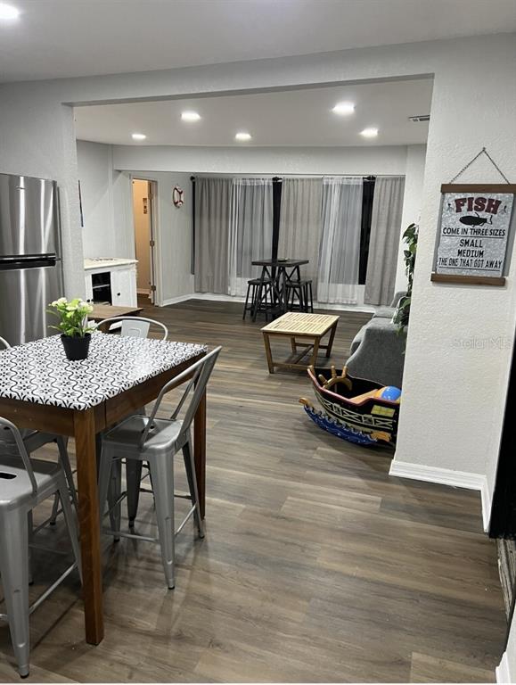 An open-concept living and dining area features wood-look flooring, a metal-topped table, and recessed lighting — 10015 LINDA STREET, GIBSONTON, FL