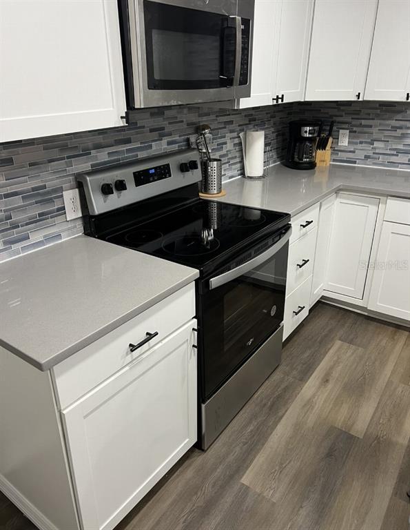 A kitchen features white cabinets, gray countertops, a glass-tile backsplash, and stainless steel appliances — 10015 LINDA STREET, GIBSONTON, FL