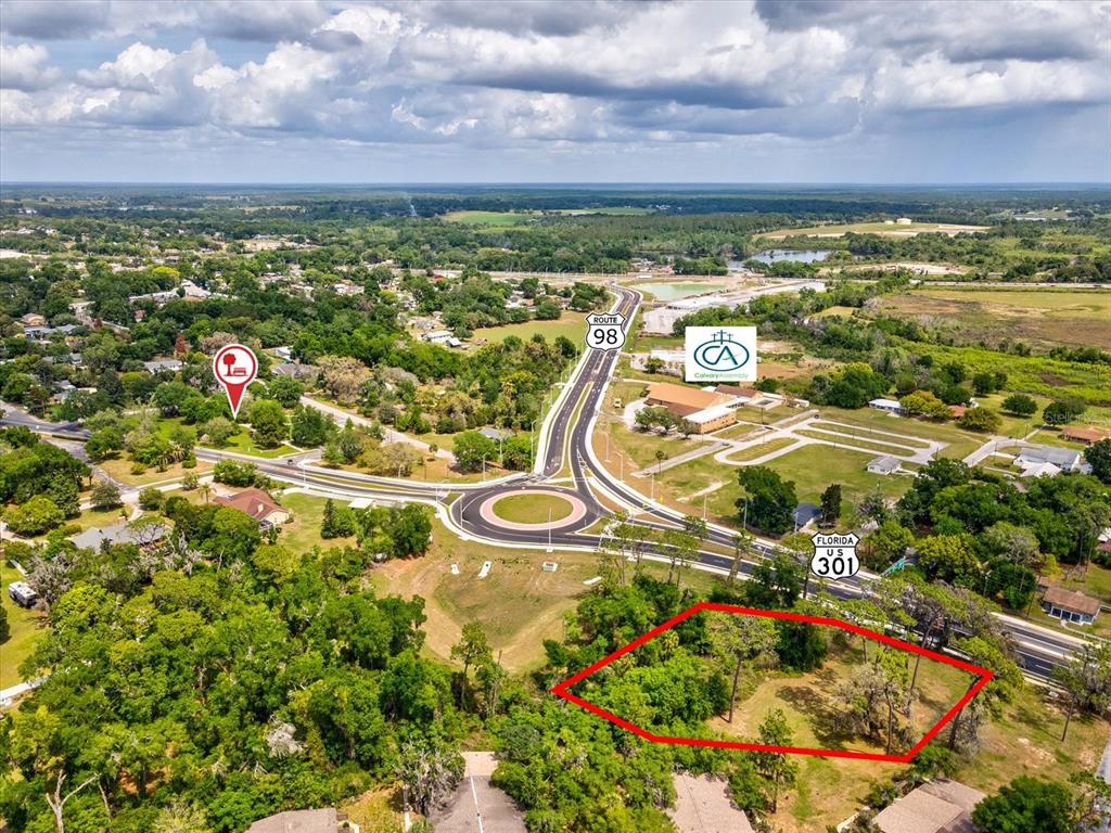 An aerial view shows a vacant, wooded lot outlined in red near a highway roundabout — STATE RD 98, DADE CITY, FL
