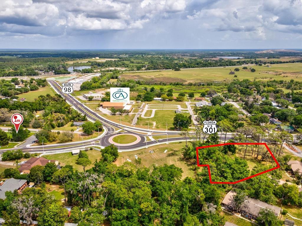 This aerial view shows a vacant, tree-covered lot outlined in red near a highway intersection — STATE RD 98, DADE CITY, FL
